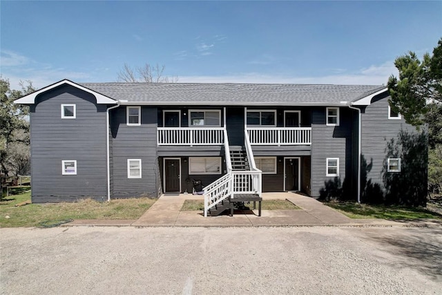 townhome / multi-family property with stairway, a porch, and roof with shingles