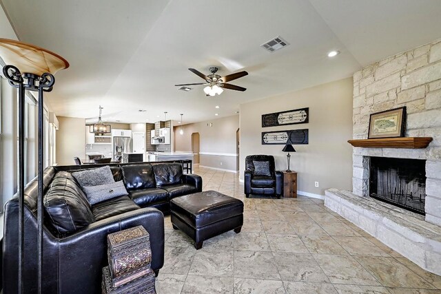 living area featuring visible vents, ceiling fan with notable chandelier, recessed lighting, a stone fireplace, and baseboards