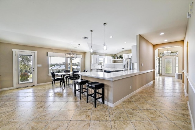 kitchen with stainless steel fridge with ice dispenser, light countertops, a peninsula, a notable chandelier, and white cabinetry