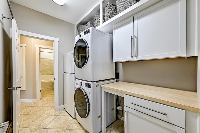 laundry area with light tile patterned flooring, stacked washer / dryer, cabinet space, and baseboards