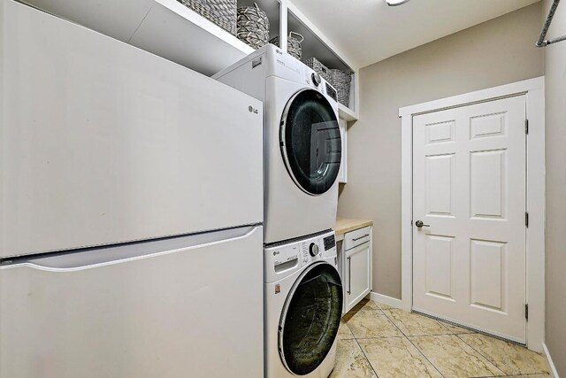 clothes washing area featuring cabinet space, stacked washer and clothes dryer, and baseboards