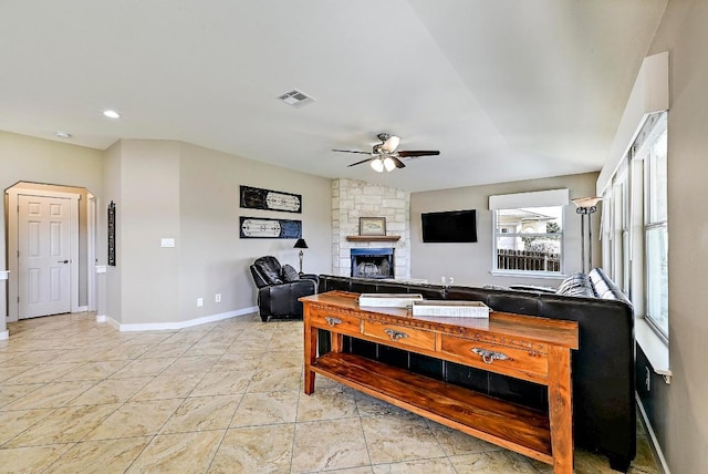 living area with visible vents, baseboards, ceiling fan, a stone fireplace, and light tile patterned flooring