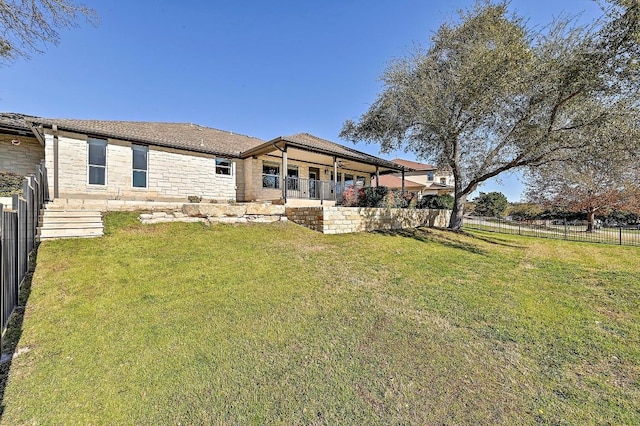 rear view of property with a patio area, a yard, fence, and stone siding