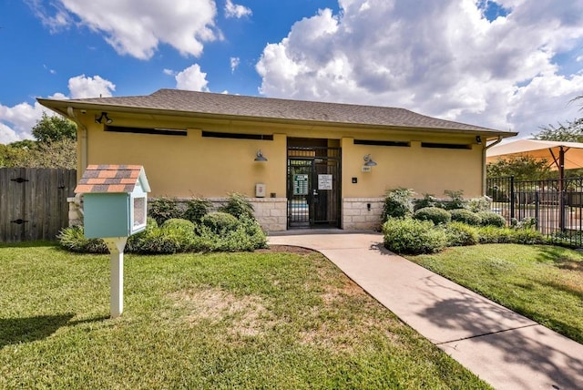 view of front facade with stucco siding, stone siding, a front lawn, and fence