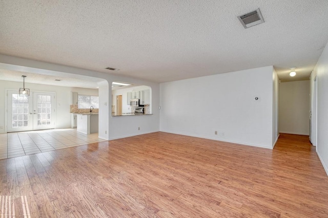 unfurnished living room featuring visible vents, baseboards, french doors, light wood-style floors, and a textured ceiling