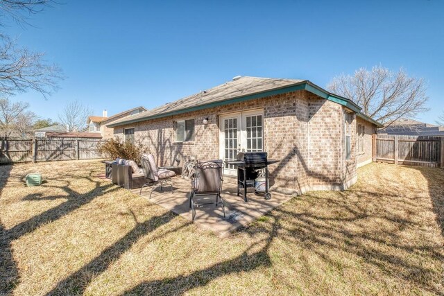 rear view of house with brick siding, a lawn, french doors, a fenced backyard, and a patio area