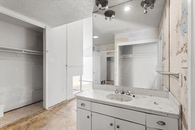 bathroom featuring vanity, a walk in closet, unfinished concrete floors, and a textured ceiling