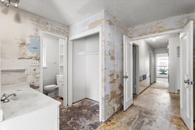 bathroom with wallpapered walls, a textured ceiling, vanity, and toilet