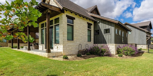 view of home's exterior featuring fence, a lawn, board and batten siding, and stone siding