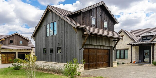 view of front of house featuring driveway, a standing seam roof, a garage, stone siding, and metal roof