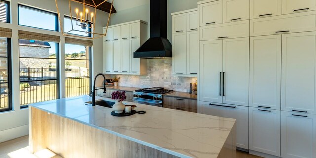 kitchen with a kitchen island with sink, a sink, high end stove, wall chimney range hood, and backsplash