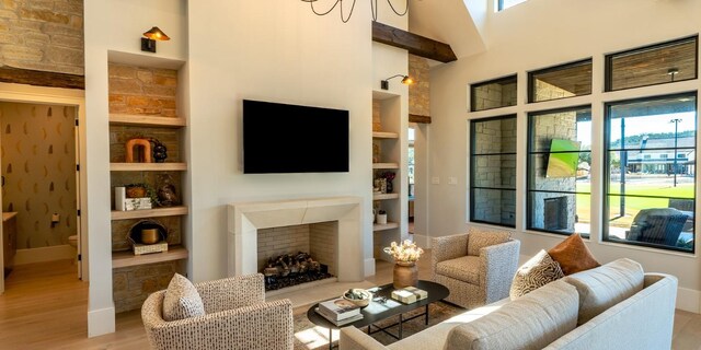 living room with built in shelves, wood finished floors, baseboards, a fireplace, and a towering ceiling