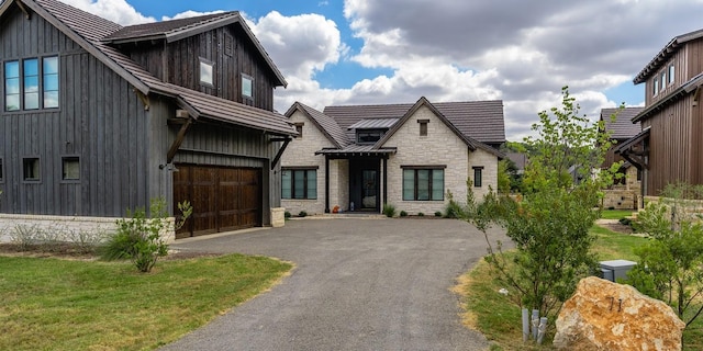 modern farmhouse featuring aphalt driveway, metal roof, a garage, stone siding, and a standing seam roof