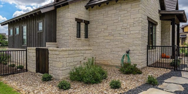 view of side of home with a gate, fence, and stone siding