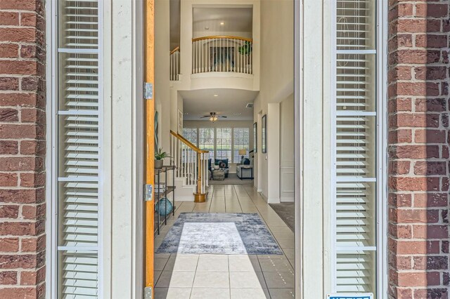 tiled foyer featuring a ceiling fan, brick wall, and stairs