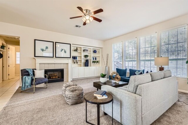 living area with tile patterned flooring, visible vents, a tile fireplace, and a ceiling fan