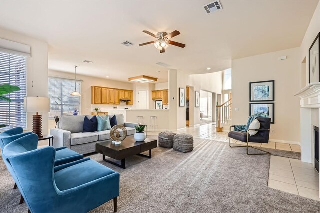 living area with visible vents, a fireplace with flush hearth, light tile patterned flooring, and a ceiling fan