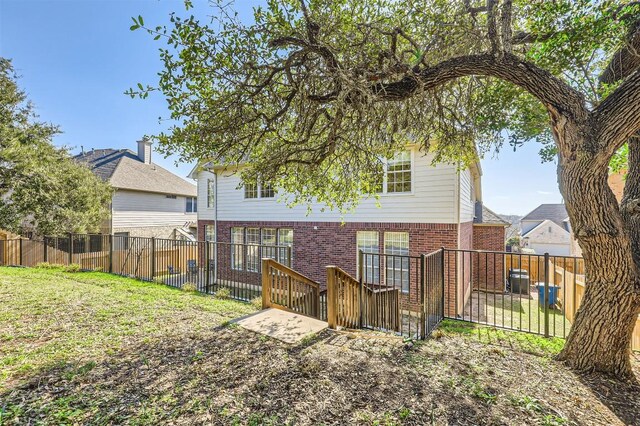 back of property with brick siding, a fenced backyard, and a yard