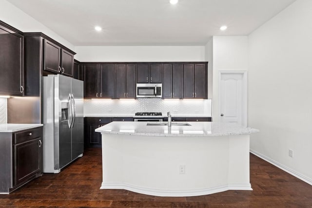 kitchen with an island with sink, a sink, tasteful backsplash, stainless steel appliances, and dark wood-style flooring