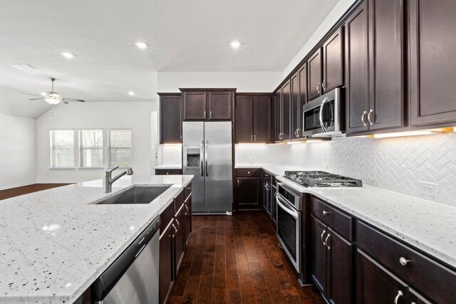 kitchen with a sink, light stone counters, appliances with stainless steel finishes, and dark wood finished floors