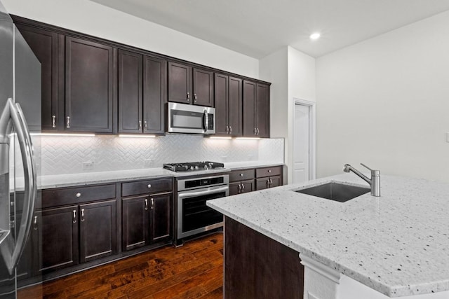 kitchen with light stone counters, dark wood finished floors, a sink, appliances with stainless steel finishes, and backsplash