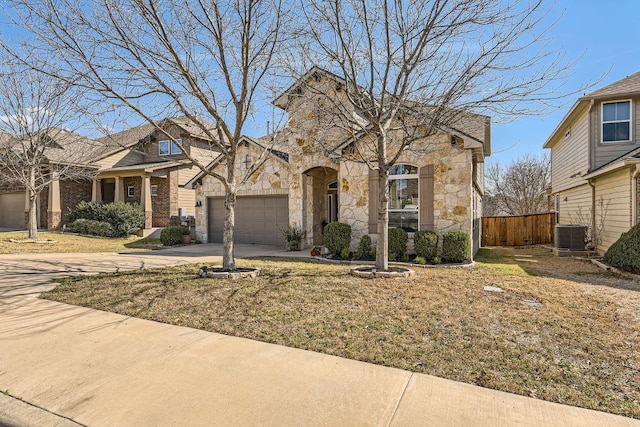 view of front of property featuring stone siding, driveway, an attached garage, and fence