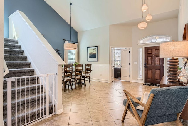 entryway with stairway, a wainscoted wall, high vaulted ceiling, and light tile patterned flooring