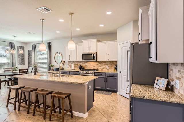 kitchen with visible vents, a kitchen bar, appliances with stainless steel finishes, light tile patterned flooring, and white cabinets