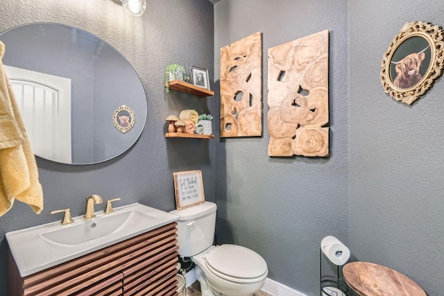 bathroom featuring vanity, toilet, a textured wall, and baseboards