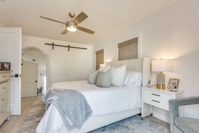 bedroom featuring a barn door, light wood-type flooring, and ceiling fan