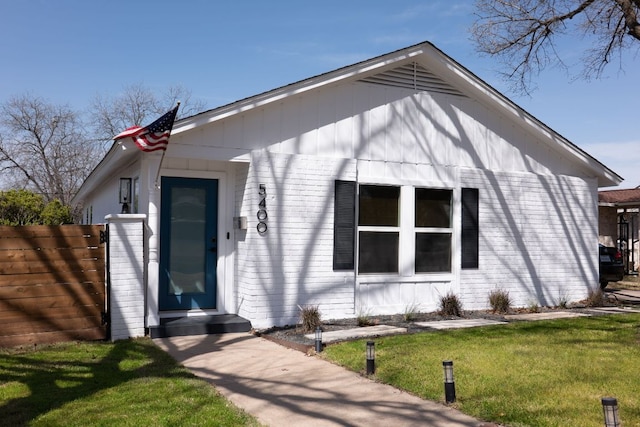 bungalow featuring brick siding, a front lawn, and fence