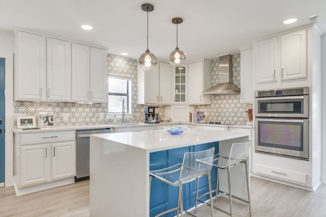 kitchen featuring wall chimney range hood, a breakfast bar, appliances with stainless steel finishes, white cabinetry, and a sink