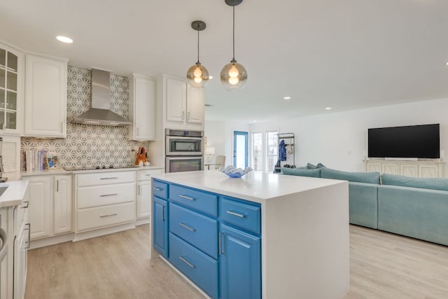 kitchen featuring white cabinets, double oven, wall chimney exhaust hood, and light wood-style floors