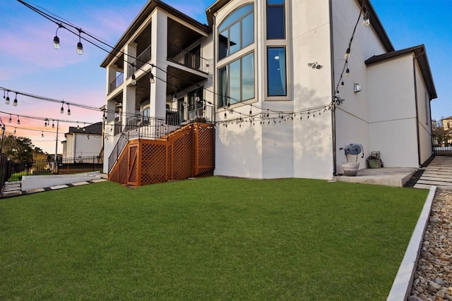 back of house at dusk featuring stairway, a lawn, fence, and stucco siding