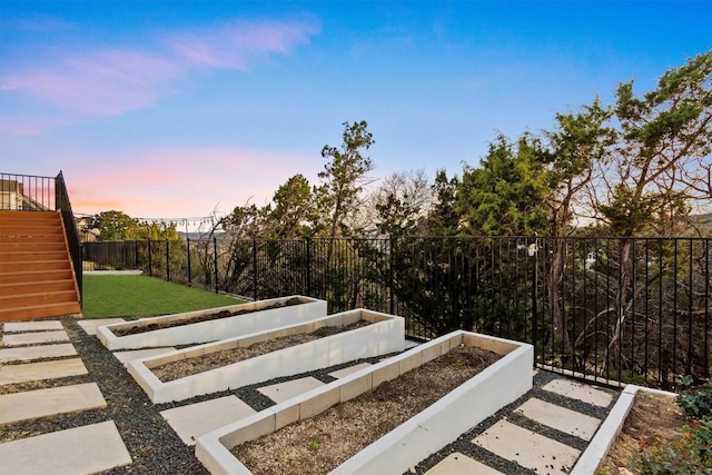 yard at dusk with stairs, a garden, and a fenced backyard