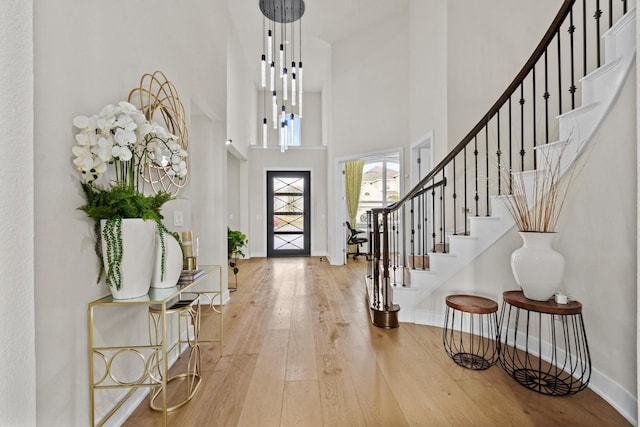 entryway with hardwood / wood-style floors, stairway, baseboards, a towering ceiling, and a chandelier