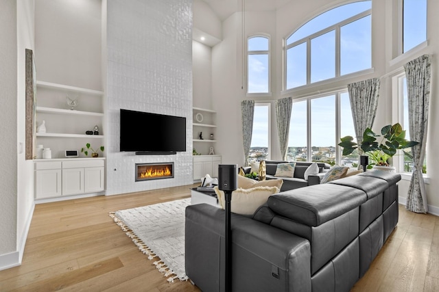 living area featuring built in shelves, baseboards, light wood-style flooring, a tile fireplace, and a towering ceiling