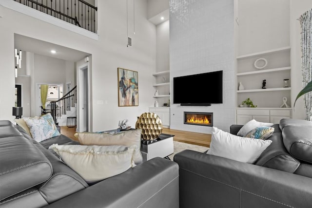 living room with a tiled fireplace, built in shelves, stairs, and wood finished floors