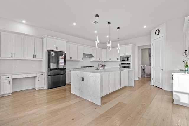 kitchen with light wood finished floors, under cabinet range hood, light countertops, appliances with stainless steel finishes, and a sink