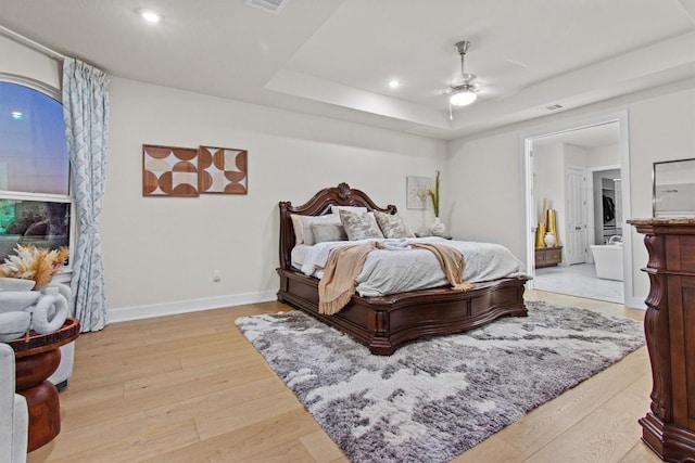 bedroom with a raised ceiling, recessed lighting, light wood-style floors, stacked washer / drying machine, and baseboards