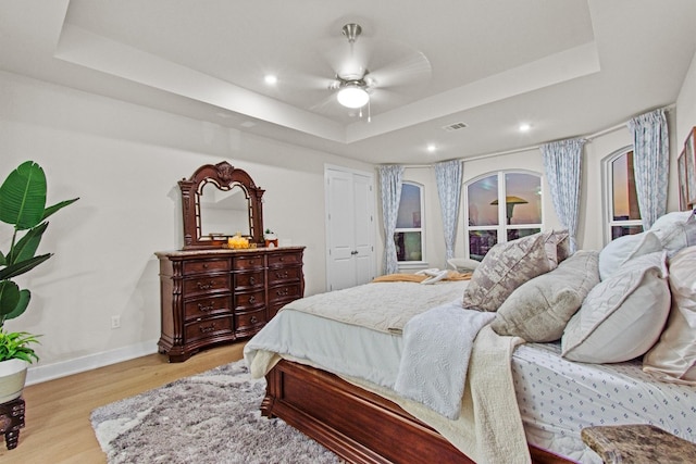 bedroom with visible vents, a raised ceiling, a ceiling fan, light wood finished floors, and baseboards