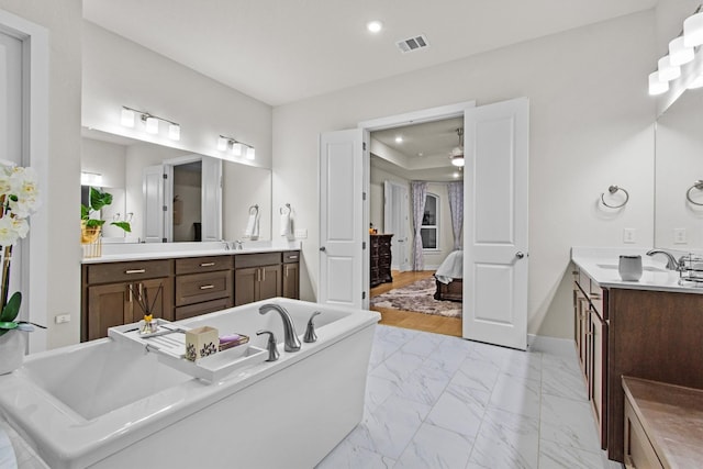 ensuite bathroom with a freestanding tub, visible vents, marble finish floor, a sink, and baseboards