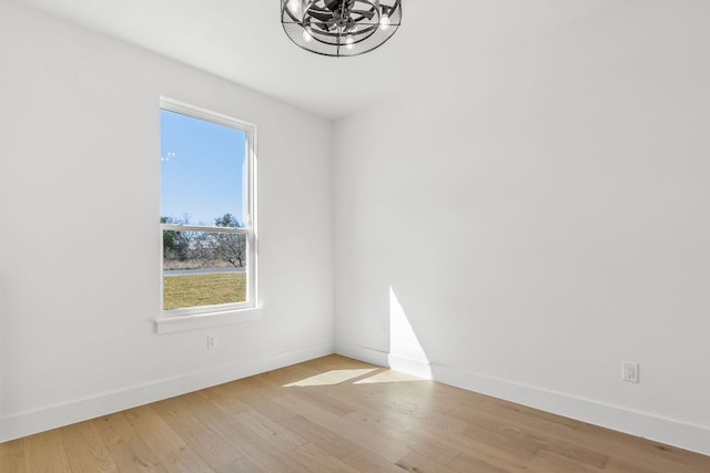 spare room with light wood-type flooring, baseboards, and an inviting chandelier