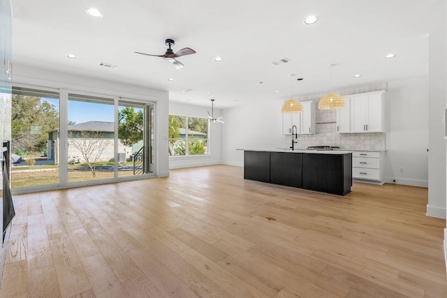 kitchen with decorative backsplash, visible vents, baseboards, open floor plan, and ceiling fan with notable chandelier