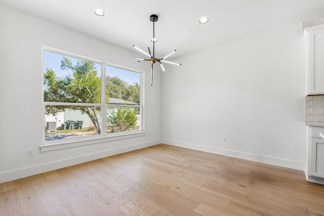 unfurnished living room featuring baseboards, light wood-type flooring, and an inviting chandelier