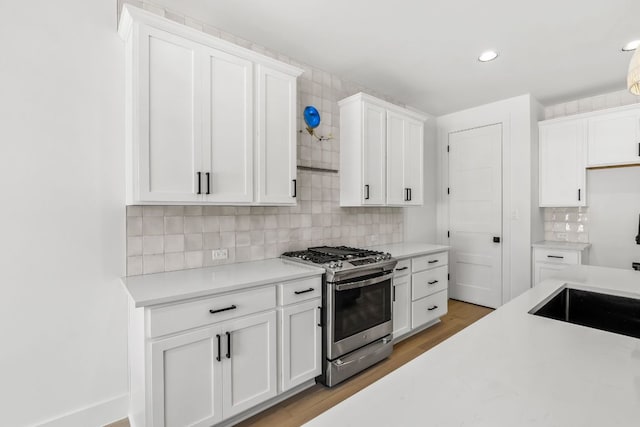 kitchen featuring backsplash, stainless steel range with gas stovetop, light wood-type flooring, light countertops, and white cabinets