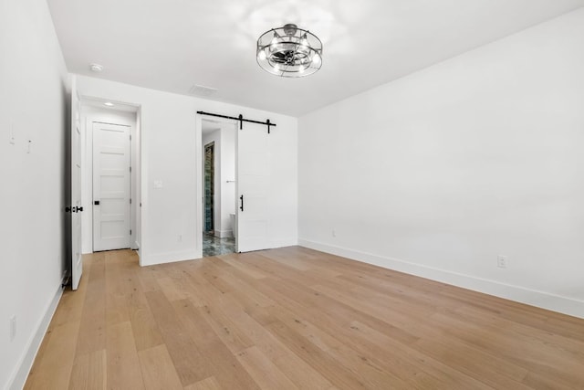 spare room with light wood finished floors, baseboards, and a barn door