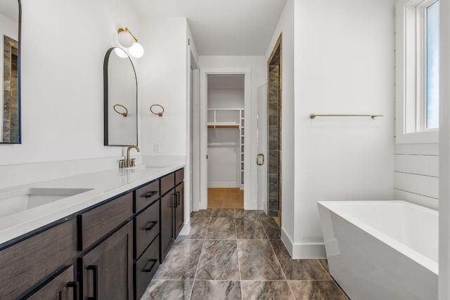 bathroom with double vanity, a soaking tub, a spacious closet, and a sink