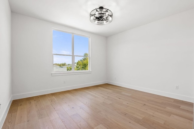 empty room with light wood finished floors, an inviting chandelier, and baseboards