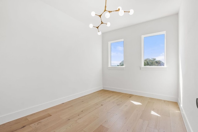 empty room with light wood-type flooring, baseboards, and a notable chandelier